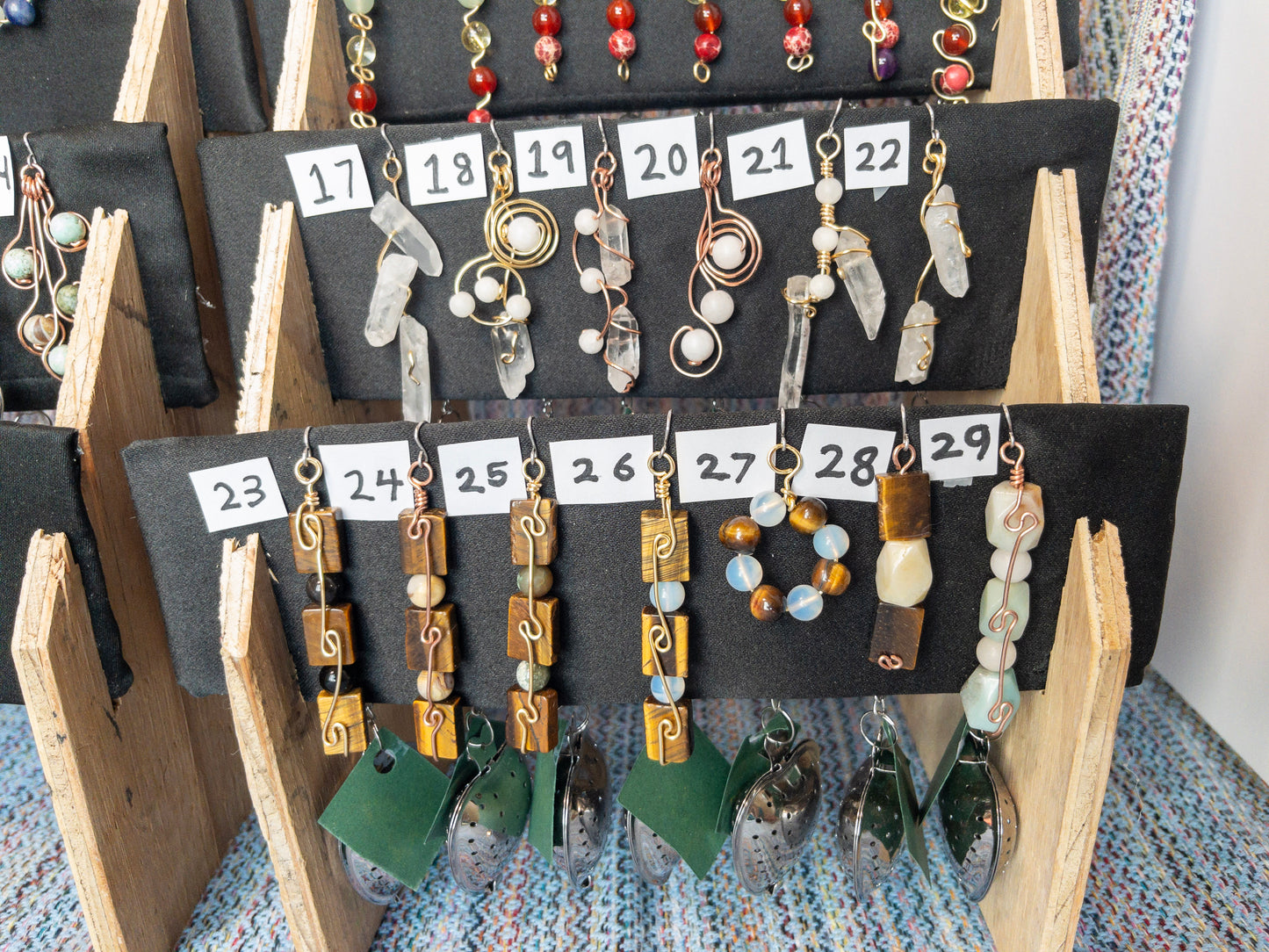 Display of various tea infusers with natural stone charms on a wooden stand.