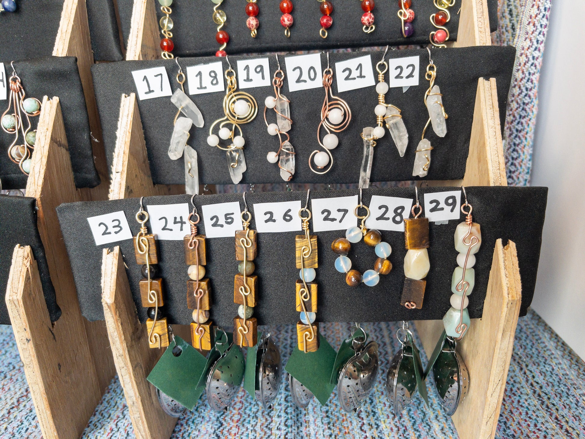 Display of various tea infusers with natural stone charms on a wooden stand.