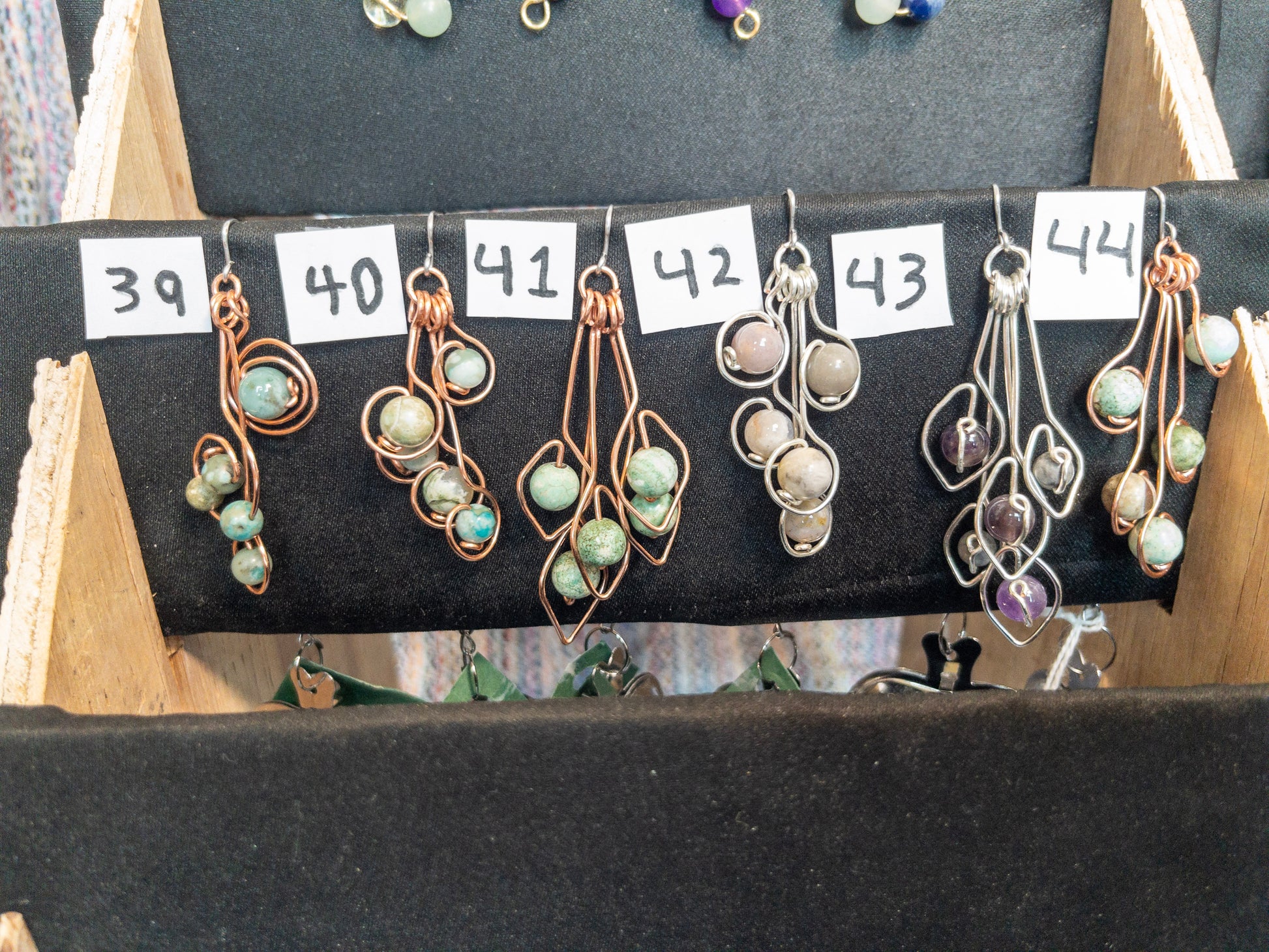 Display of various tea infusers with natural stone charms on a wooden stand